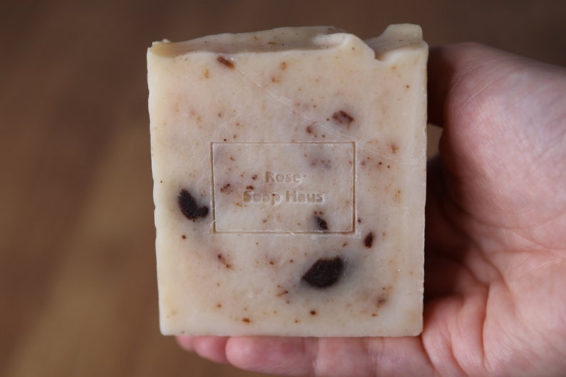 May include: A white bar of soap with brown flecks and the text "Rose Soap Haus" stamped on the front.