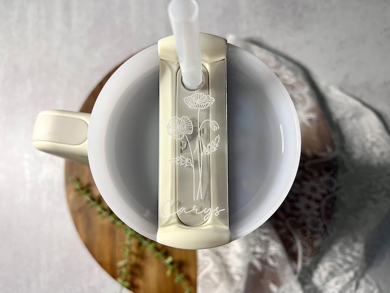 May include: White travel mug with a straw and a floral design on the lid. The lid has a sliding cover to protect the straw. The mug is engraved with the name "Carys".