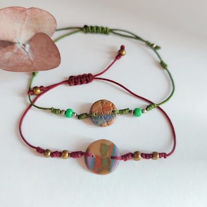 Puede incluir: Tres pulseras hechas a mano con cierres de macramé ajustables. Las pulseras presentan cuentas redondas de arcilla polimérica coloridas y pequeñas cuentas doradas. Los cordones son en tonos verdes y burdeos.