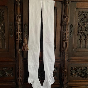Puede incluir: Un par de calcetines blancos lisos por encima de la rodilla hechos de una tela suave y opaca. Los calcetines presentan una textura de punto acanalado en la zona del pie y el talón, con las letras XL claramente visibles en negro.
