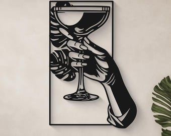 May include: Black metal wall art depicting a hand holding a stemmed glass, possibly a cocktail or wine glass. The art piece is set within a rectangular frame and features a minimalist design. The background is a neutral color, and the art is displayed above a sofa.
