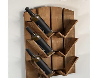 May include: A wooden wall-mounted wine rack with three bottles of wine. The rack is made of natural wood with a rustic finish. The bottles are arranged in a staggered pattern, with the necks of the bottles facing outward.