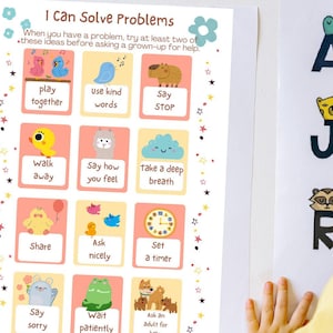Op de afbeelding: Twee educatieve posters worden op een witte muur weergegeven. Eén poster leest "Ik kan problemen oplossen" met geïllustreerde probleemoplossingsstappen. De andere poster toont het alfabet met dierenillustraties. Een kind in een gele jurk staat in de buurt van de posters.