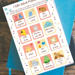May include: A colorful educational chart titled "I Can Solve Problems" with illustrated tips like "Play Together" and "Use Kind Words." The chart is on top of a blue notebook, promoting social-emotional learning for children.