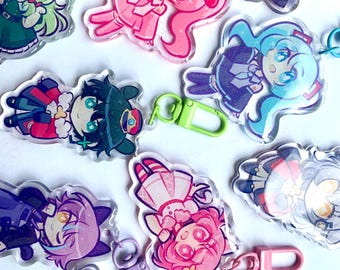 Puede incluir: Una colección de diez llaveros de acrílico transparente con diferentes personajes de anime. Los llaveros están decorados con purpurina y presentan diferentes colores, como rosa, azul, verde y morado.