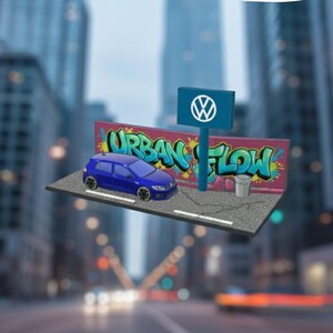 Op de afbeelding: Een blauw Volkswagen-automodel staat op een miniatuur straatbeeld met een graffiti-muurschildering met de tekst "URBAN FLOW". Een bord met het Volkswagen-logo is zichtbaar. De achtergrond toont een vage stadsgezicht.