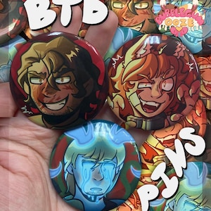 Op de afbeelding: Een verzameling ronde pins met kleurrijke illustraties van personages in anime-stijl. De pins hebben een glanzende afwerking en zijn in tinten rood, bruin, geel en blauw. De tekst "BTD" en "PINS" is zichtbaar.