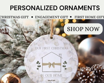 Może przedstawiać: Spersonalizowana ceramiczna ozdoba z napisem "OUR FIRST CHRISTMAS IN OUR HOME". Ozdoba przedstawia grafikę domu z kokardą i liśćmi eukaliptusa. Tekst "Jane & Jack" i data "June 26th 2023" są również uwzględnione. Konfigurowalny prezent.