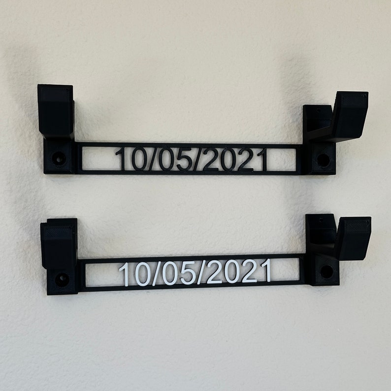 Pode incluir: Dois suportes de parede de metal preto com a data "10/05/2021" impressa neles.