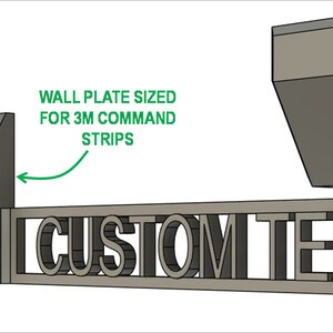 Pode incluir: Um suporte de parede de metal cinza com dois ganchos angulares e um espa&ccedil;o para texto personalizado. Os ganchos t&ecirc;m furos para montagem com pregos ou tiras de comando 3M. A &aacute;rea de texto tem furos de parafuso embutidos com tampas para ocult&aacute;-los.