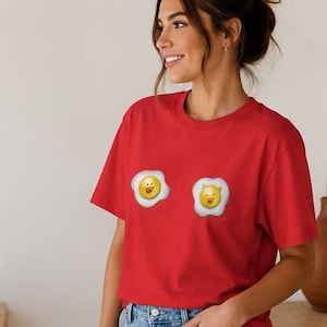 Può includere: Una maglietta rossa con due uova fritte a fumetto con facce sorridenti. Le uova sono gialle con albumi bianchi. La maglietta è a maniche corte e realizzata in un tessuto morbido.