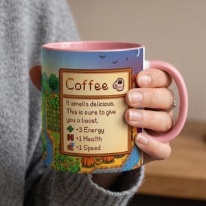 May include: A ceramic coffee mug with a pink handle and interior. The mug features a pixelated design with the word "Coffee" and text that reads "It smells delicious. This is sure to give you a boost. +3 Energy, +1 Health, +1 Speed."