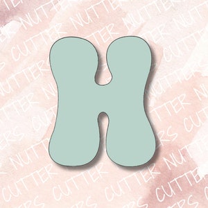 Op de afbeelding: Een lichtblauwe koekjesuitsteker in de vorm van de letter H. De uitsteker heeft een afgerond, bubbelvormig ontwerp.