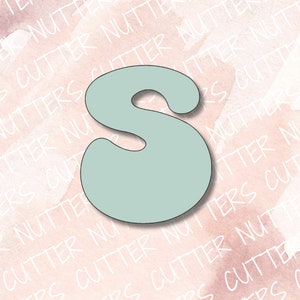 May include: A light blue plastic cookie cutter shaped like the letter S. The cutter has a rounded, whimsical design.