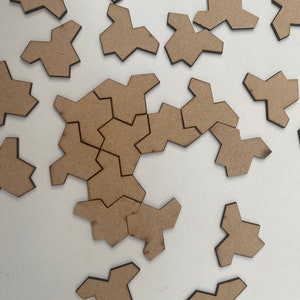 Peut inclure: Un ensemble de pièces de puzzle en bois brun en forme d'étoiles irrégulières. Les pièces sont éparpillées sur une surface blanche.