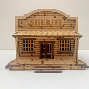 Peut inclure: Un modèle en bois d'un bâtiment de bureau de shérif de style western avec une enseigne indiquant "SHERIFF". Le bâtiment possède un porche avec une balustrade en bois et deux fenêtres de chaque côté. Le bâtiment est en bois et a une teinte brune.