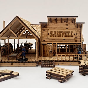 Puede incluir: Modelo de madera de un aserradero con la palabra "SAWMILL" tallada en la parte delantera. El modelo incluye figuras en miniatura, una rueda hidráulica y pilas de tablones de madera. El edificio tiene un aspecto rústico y desgastado.