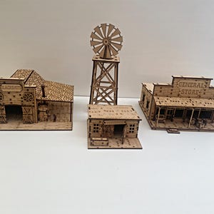 Peut inclure: Trois bâtiments en bois miniatures, une forge, une épicerie générale et un moulin à vent, tous dans un style rustique.