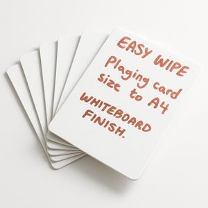 Puede incluir: Un montón de tarjetas rectangulares blancas con esquinas redondeadas. La tarjeta superior tiene texto escrito a mano en marrón rojizo: "EASY WIPE, Playing card size to A4, WHITEBOARD FINISH."