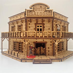 Op de afbeelding: Een houten model van een Western saloon met een bord waarop "West Saloon" staat. De saloon heeft twee verdiepingen en een balkon. Er staan twee figuren voor de saloon.
