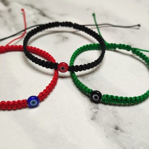 May include: Three string bracelets with evil eye charms. The bracelets are red, black, and green.