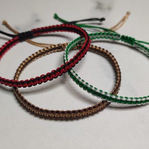 May include: Four braided bracelets in red and black, green and white, and brown. The bracelets are tied together and the text "Choose your own colours" is visible in the bottom right corner of the image.
