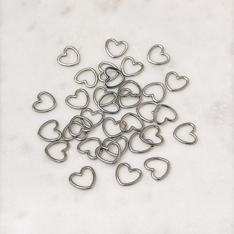 May include: A large group of silver heart-shaped jump rings. The rings are scattered on a white surface.
