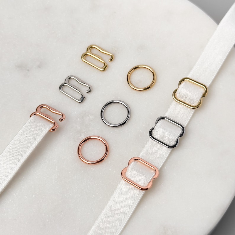 Puede incluir: Surtido de reguladores de tirantes de sujetador de metal en acabados dorado, plateado y oro rosa. Los reguladores son de diferentes formas, incluyendo cuadradas y rectangulares.