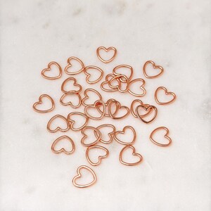May include: A pile of rose gold heart-shaped metal charms. The charms are small and delicate, perfect for adding a touch of elegance to jewelry or crafts.