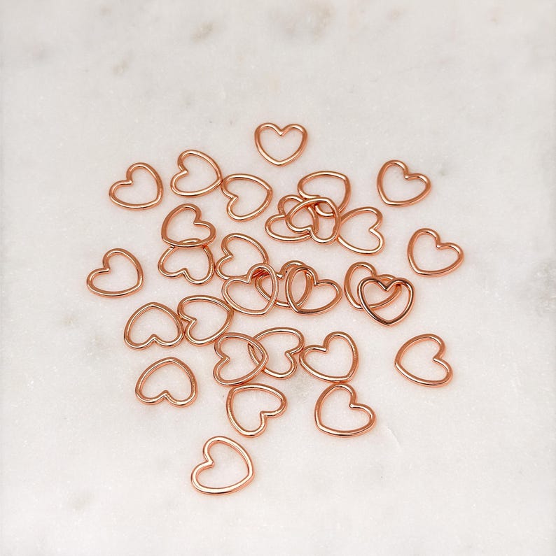 May include: A pile of rose gold heart-shaped metal charms. The charms are small and delicate, perfect for adding a touch of elegance to jewelry or crafts.