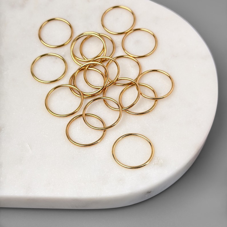 May include: A collection of gold jump rings, a type of jewelry finding, on a white marble surface.