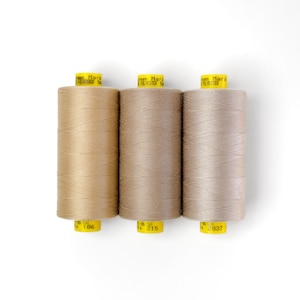Puede incluir: Tres carretes de hilo marrón con etiquetas amarillas. Las etiquetas dicen "Gütermann Mara 100% Polyester" y tienen los números de color 186, 215 y 2037.