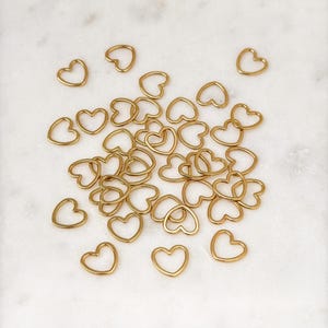 May include: A large group of gold heart-shaped metal rings. The rings are scattered on a white marble surface.