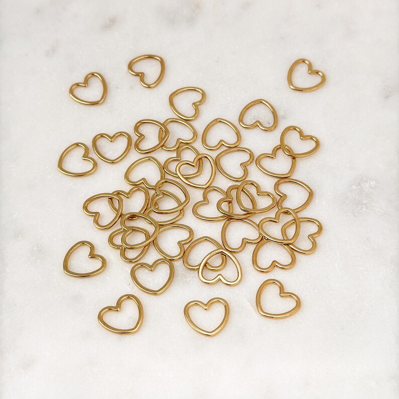 May include: A large group of gold heart-shaped metal rings. The rings are scattered on a white marble surface.