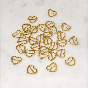 May include: A group of gold heart-shaped metal clasps scattered on a white marble surface.