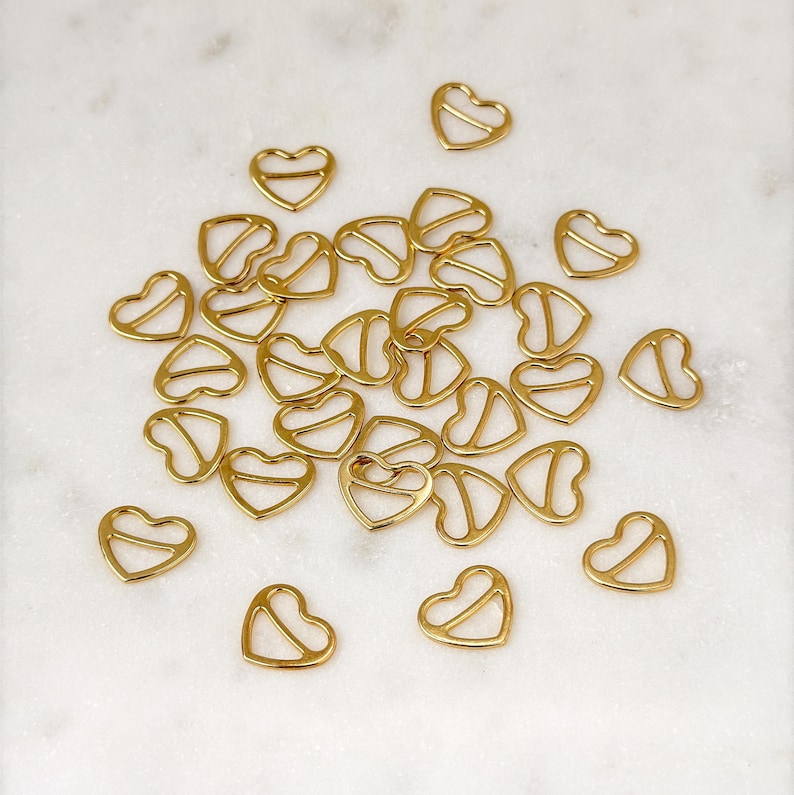 May include: A group of gold heart-shaped metal clasps scattered on a white marble surface.