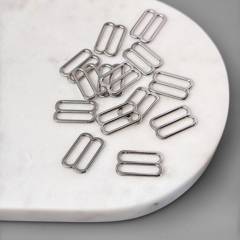May include: A pile of silver metal slider buckles, commonly used for adjusting the length of straps on clothing or bags.