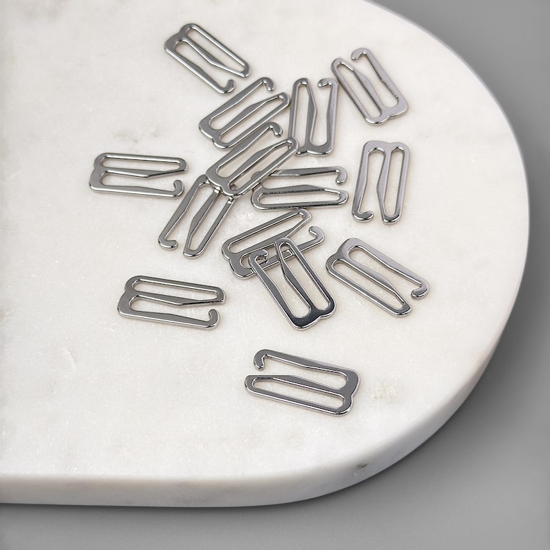 May include: A close-up of a group of silver bra strap extenders scattered on a white marble surface.