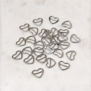 May include: A pile of silver heart-shaped metal bra strap adjusters.