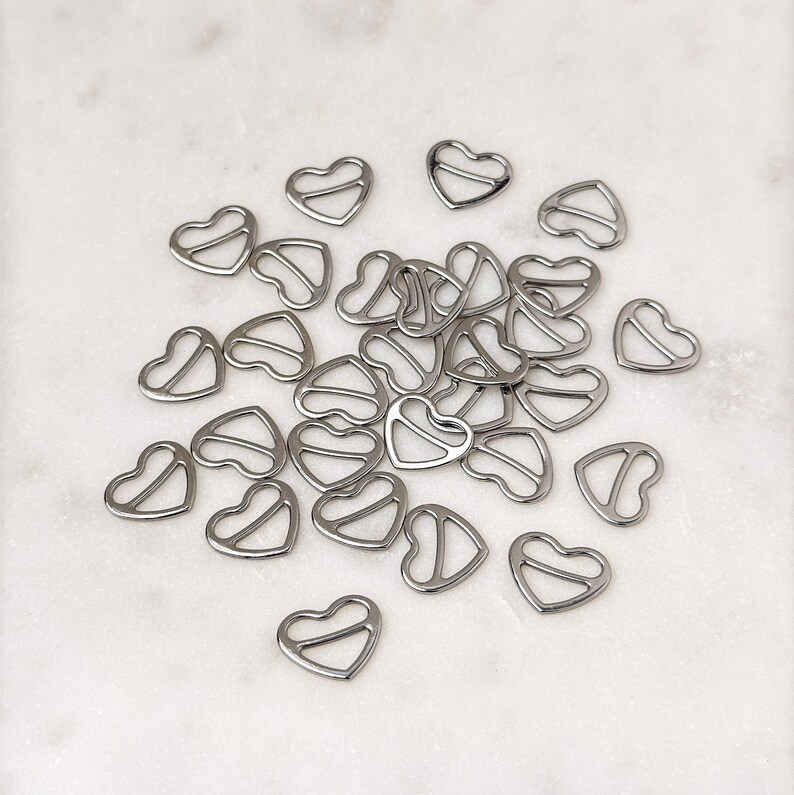May include: A pile of silver heart-shaped metal bra strap adjusters.
