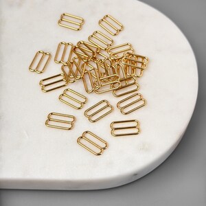 Peut inclure: Un tas de boucles coulissantes en m&eacute;tal dor&eacute;. Les boucles sont toutes de la m&ecirc;me taille et de la m&ecirc;me forme, et elles sont dispos&eacute;es de mani&egrave;re al&eacute;atoire.