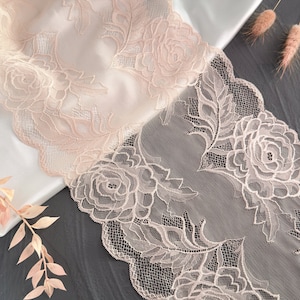 May include: A close-up of delicate, pale pink lace trim with a floral pattern. The lace features intricate designs of roses and leaves.