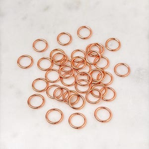 Puede incluir: Una gran cantidad de peque&ntilde;os anillos de salto de oro rosa. Los anillos est&aacute;n dispersos sobre una superficie de m&aacute;rmol blanco.