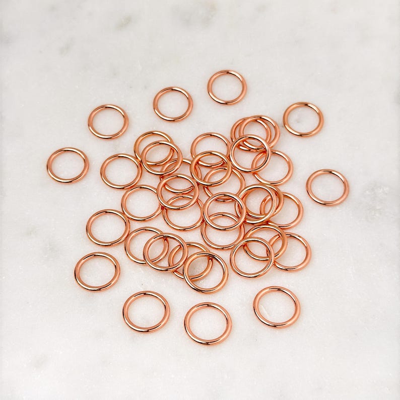 Puede incluir: Una gran cantidad de peque&ntilde;os anillos de salto de oro rosa. Los anillos est&aacute;n dispersos sobre una superficie de m&aacute;rmol blanco.