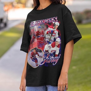 Könnte beinhalten: Ein schwarzes T-Shirt mit einem Grafikdruck des Eishockeyspielers Juraj Slafkovsky in verschiedenen Posen, der ein rot-weißes Trikot trägt. Der Text SLAFKOVSKY ist in großen blauen und roten Buchstaben gedruckt, darunter der Name Juraj in Schreibschrift.
