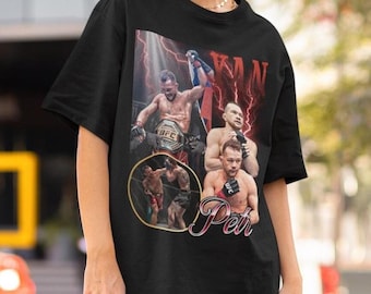 May include: A black short-sleeve t-shirt featuring a graphic print of a mixed martial arts fighter in various poses, including holding a championship belt. The design includes red lightning accents and the text "YAN" and "Petr" in stylized fonts.