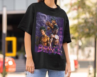 May include: Black t-shirt with a graphic print of three men in martial arts poses. The graphic is in a retro style with purple and pink accents. The text "Bruce Lee" is printed below the graphic.