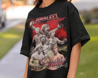 May include: A black short-sleeve t-shirt featuring a graphic collage of mixed martial artist Paddy Pimblett. The design includes the text PIMBLETT THE BADDY and Paddy in a stylized red and white font, set against a red and gold background.
