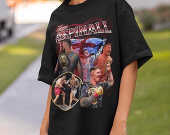 May include: Black t-shirt with a graphic print of Tom Aspinall, a mixed martial arts fighter. The graphic features Aspinall in a fighting pose with other fighters and a championship belt.