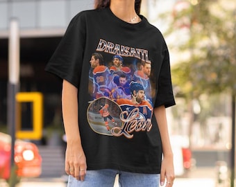 May include: Black t-shirt featuring a collage of hockey player images with the name "Draisaitl" in orange and blue. The shirt also includes the name "Leon" in a script font, and images of the player in action.